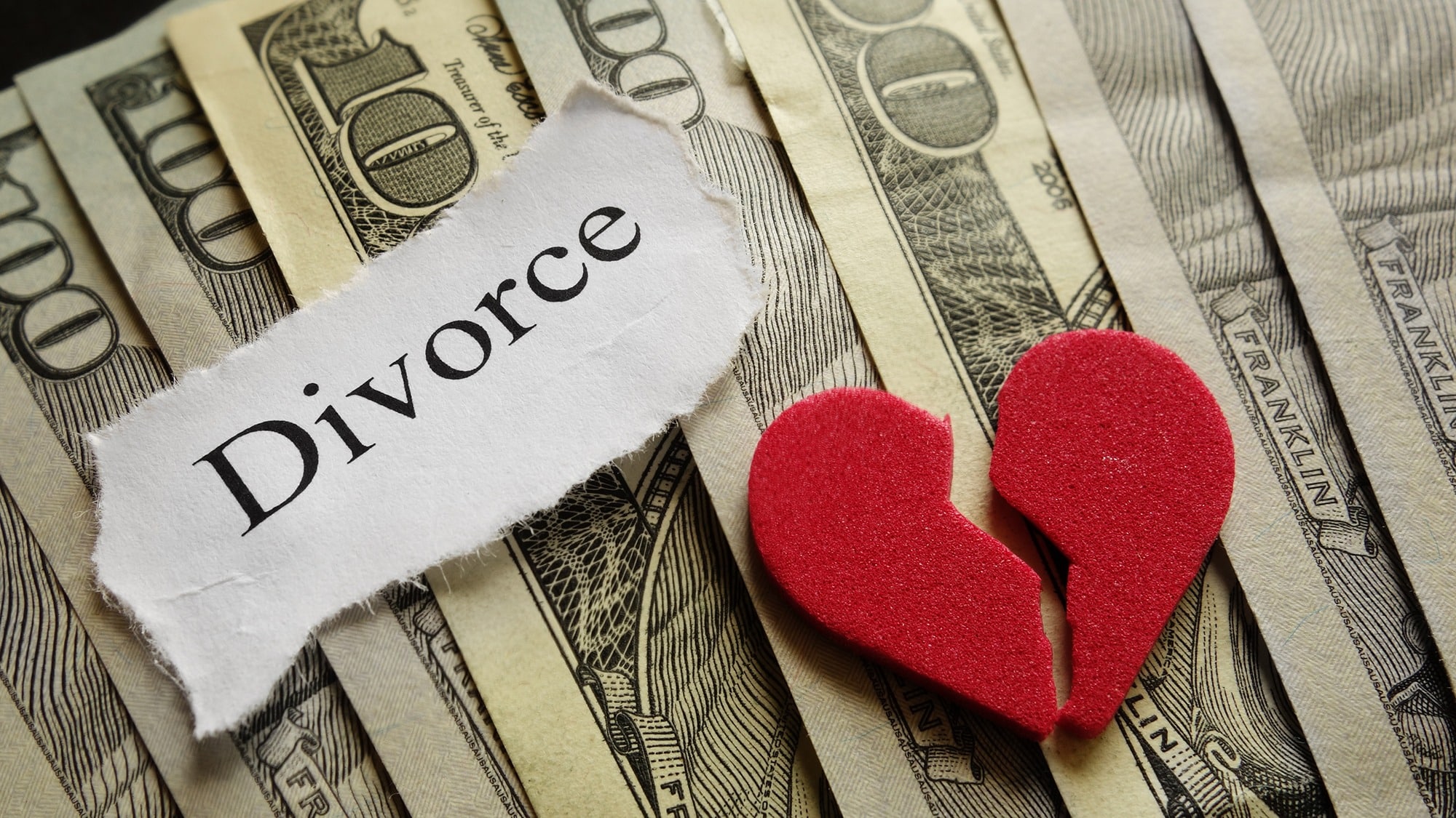 Torn divorce paper and broken heart on dollar bills symbolising financial cost of separation