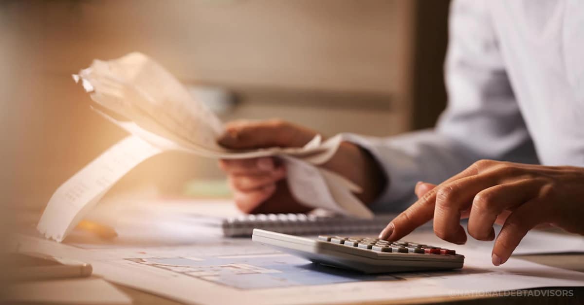 Close-up of hands using a calculator and reviewing financial documents on a desk.